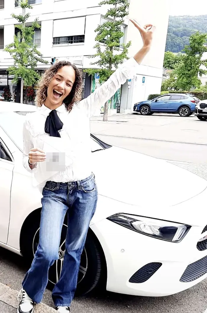 Fahrschülerin freut sich mit ihrem Ausweis neben dem Schulungsauto